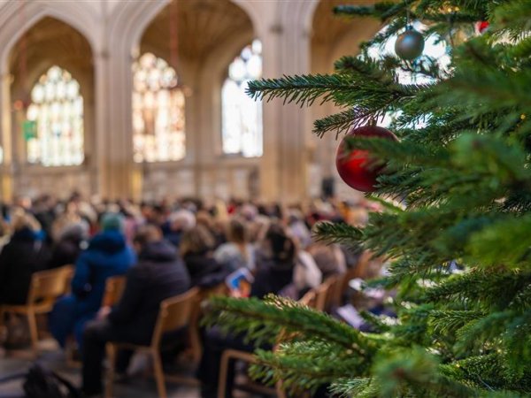 Part of a Christmas tree with a group of people sitting behind for a church service at Bath Abbey