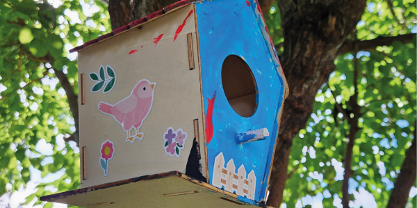 Blue and wooden painted nest box, covered in children's stickers up in a tree.