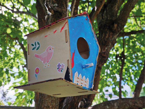 Blue and wooden painted nest box, covered in children's stickers up in a tree.