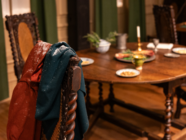 A pair of coats dusted with snow rest on the back of an old wooden chair.