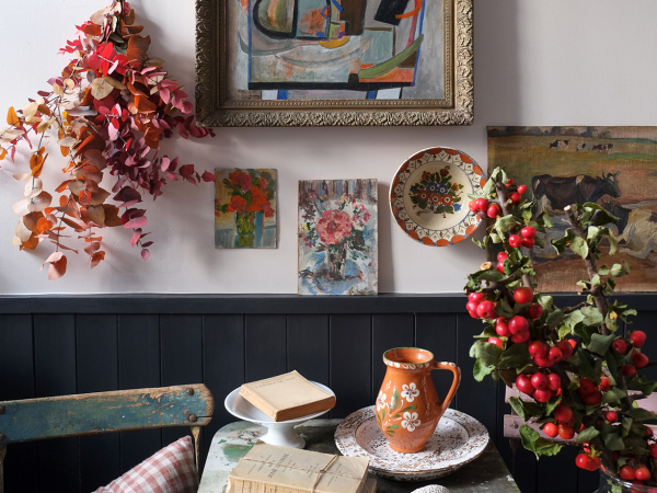 Part of a room decorated with greenery, bowls and books on a table and paintings on the wall