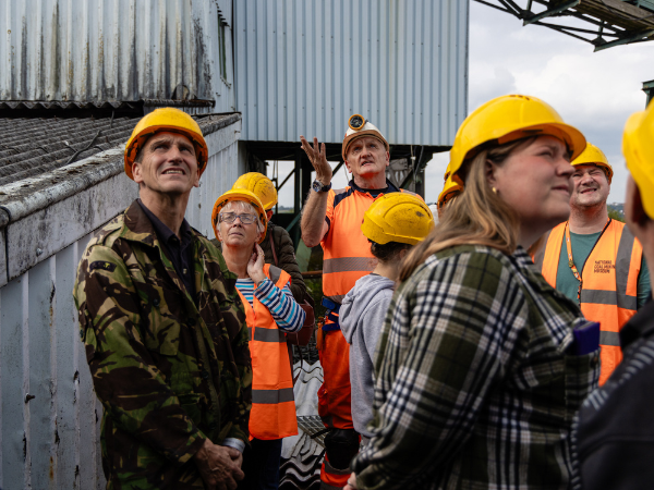 A miner leading a tour of the Screens Building with a group wearing hard hats