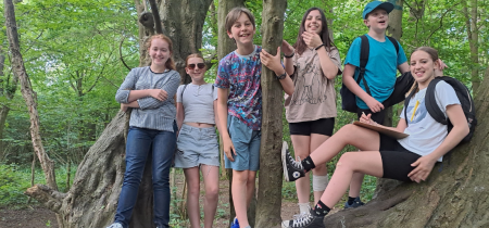 Young people stand, smiling on a tree in a woodland