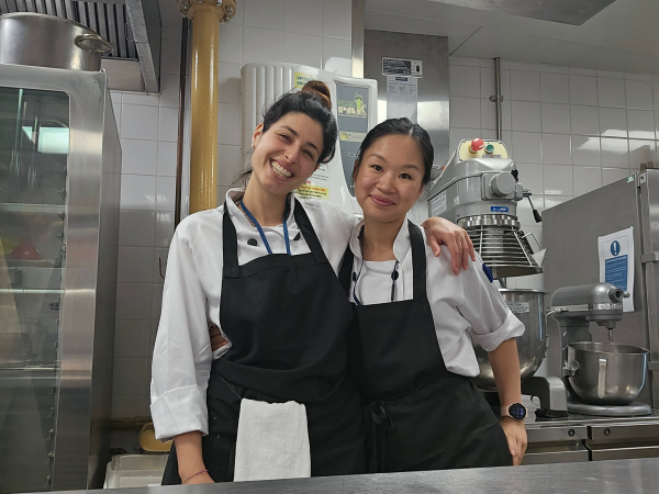 Two female-presenting chefs stand smiling together