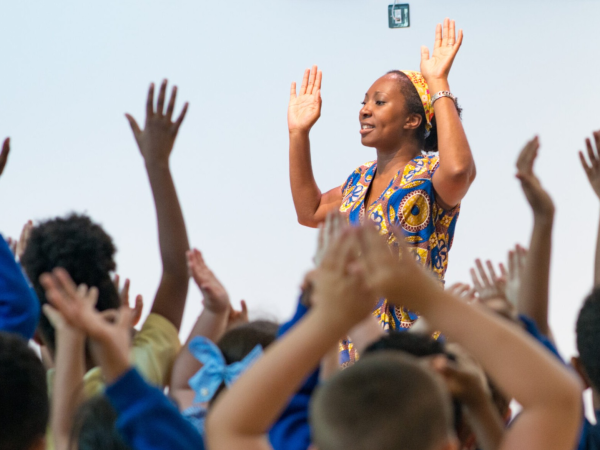 A performer with arms raised expressively, behind lots of other raised arms in an audience.
