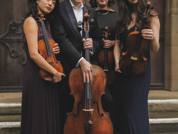 Four people dressed all in black, holding string instruments.