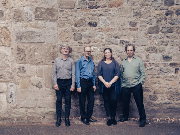Four people stood against a brick wall, smiling.