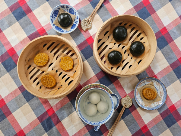 Bowls and bamboo steamers full of sweet treats, against a colourful checked tablecloth