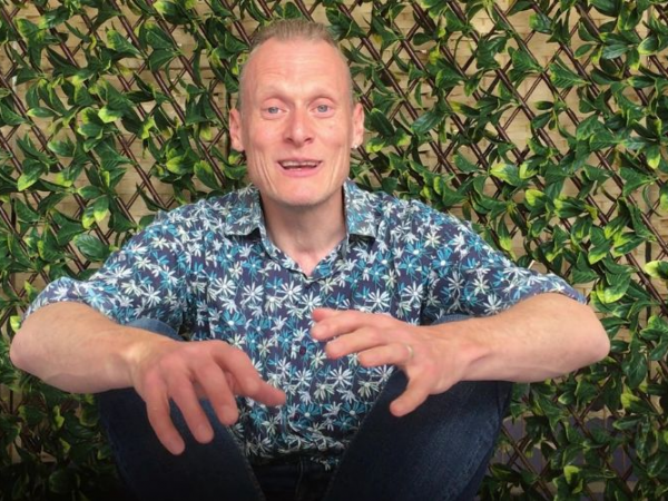 Mike Dodsworth learns towards the camera to tell you a story. He sits in front of a green leafy background