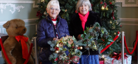 Two women in front of a Christmas tree. holding Christmas wreaths