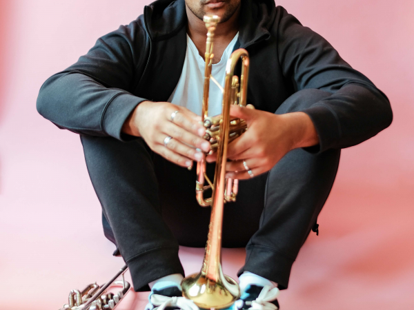 A man holding a trumpet, sat in a pink room.