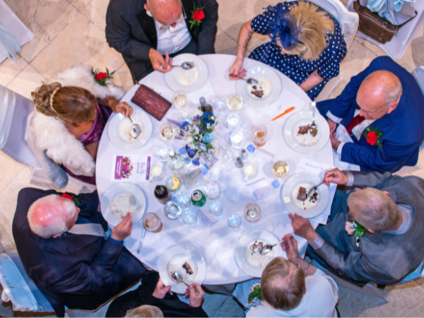 A table of people eating in a formal dinner setting with the photo taken from above