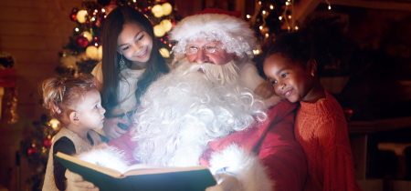 Jolly Santa reads a story to 3 children who are gathered round him