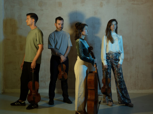 Four people in muted clothing standing in a concrete building.