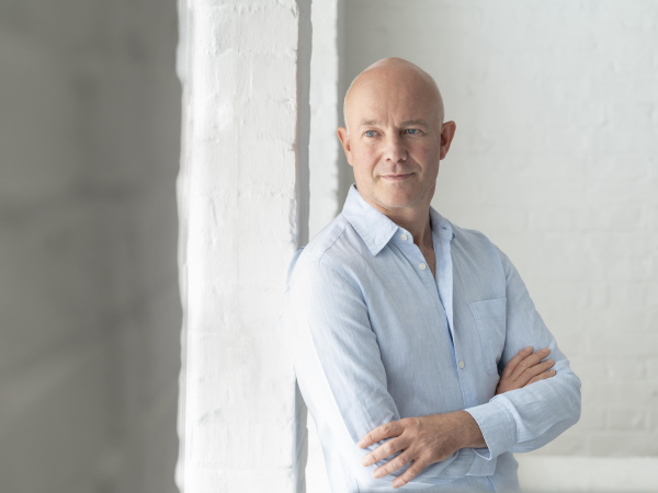 A man in a light blue shirt leaning beside a window.