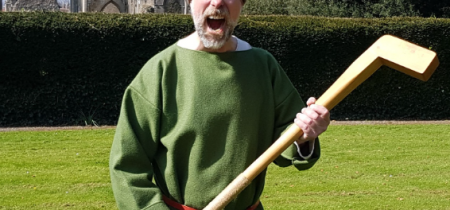 A man in historic costume holding a wooden tool and shouting.