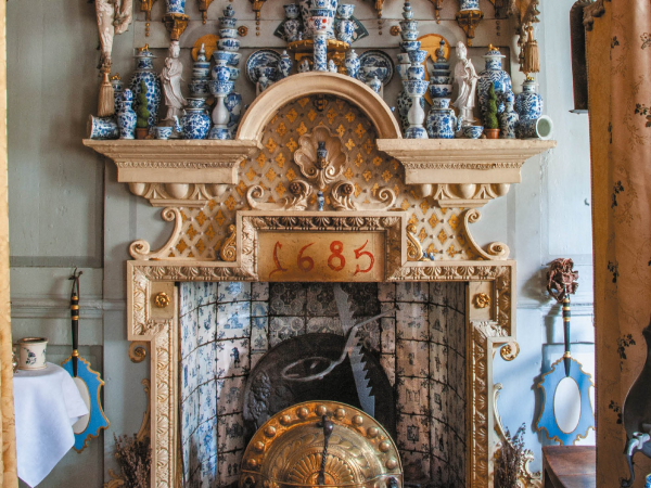 An ornate stone and tile fireplace, dated 1685, with plenty of blue and white urns and bowls stacked high on the mantlepiece