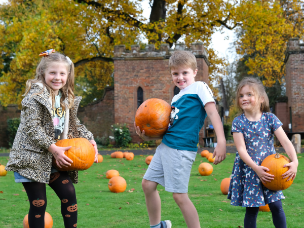 Two girls and a boy outside Hartlebury Castle holding pumpkins