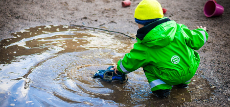 A child plays with a toy car in a muddy puddle.