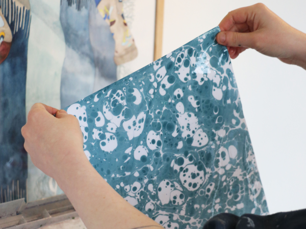 Two hands holding up a sheet of blue and white marbled paper