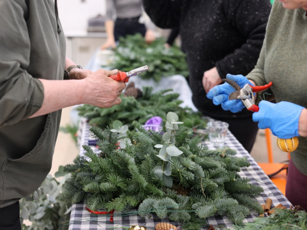 A pair of hands holds a Christmas wreath over a rustic festive table.