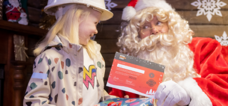 A young girl meeting Santa and receiving a gift and certificate.