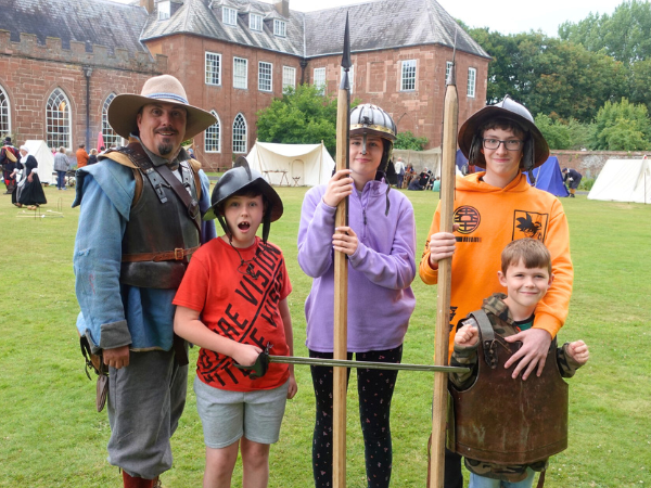 A man and four boys outside Hartlebury Castle, holding pikes and swords and wearing armour