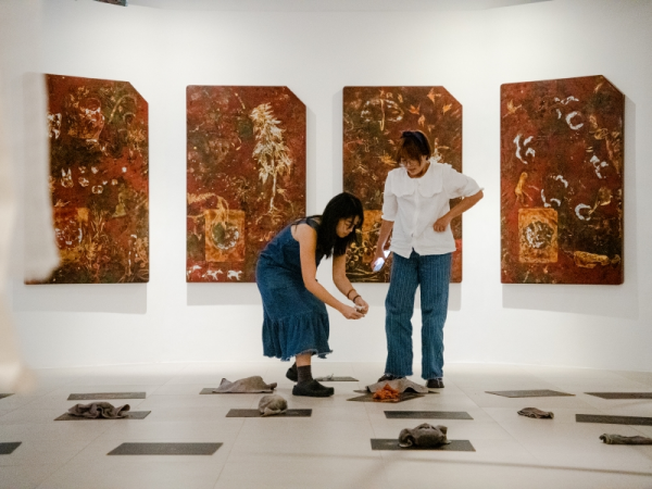 Two people prepare workshop materials in a room with four large red artworks.