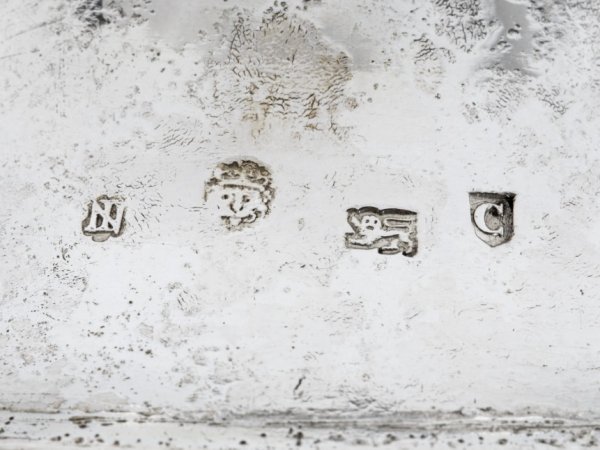 A close up of 4 hallmarks on an aged silver object