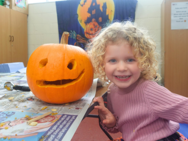 Smiling girl posing next to a carved pumpkin with a Halloween banner in the background