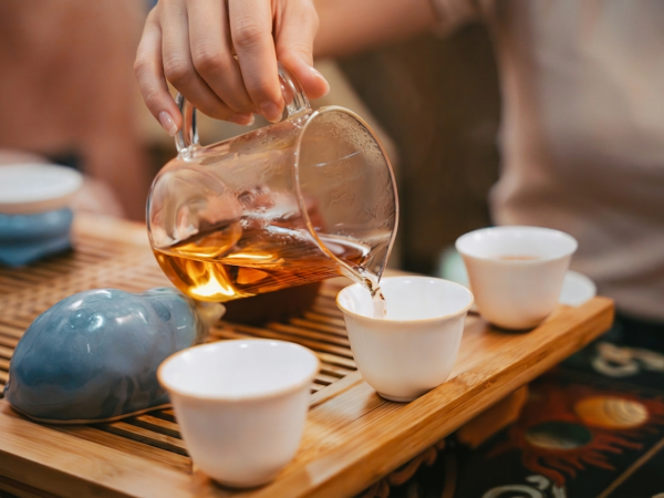 A photograph of a hand pouring tea into ceramic cups
