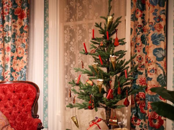 A Christmas tree and upholstered chair in a Victorian room with decorative curtains