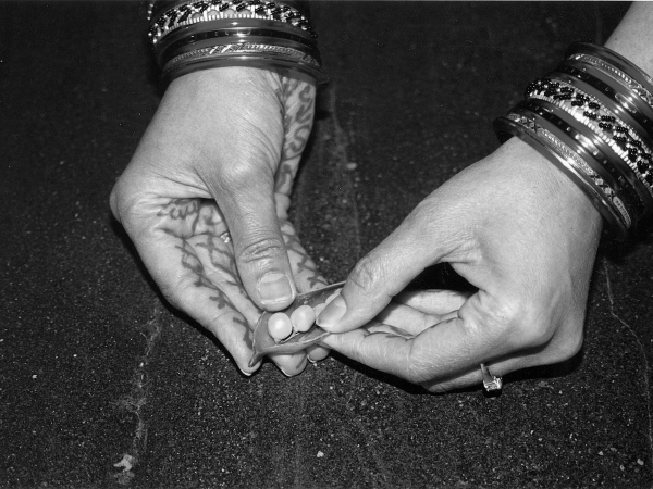 A pair of hands, with henna decoration and bangles, carefully opening a pod of peas